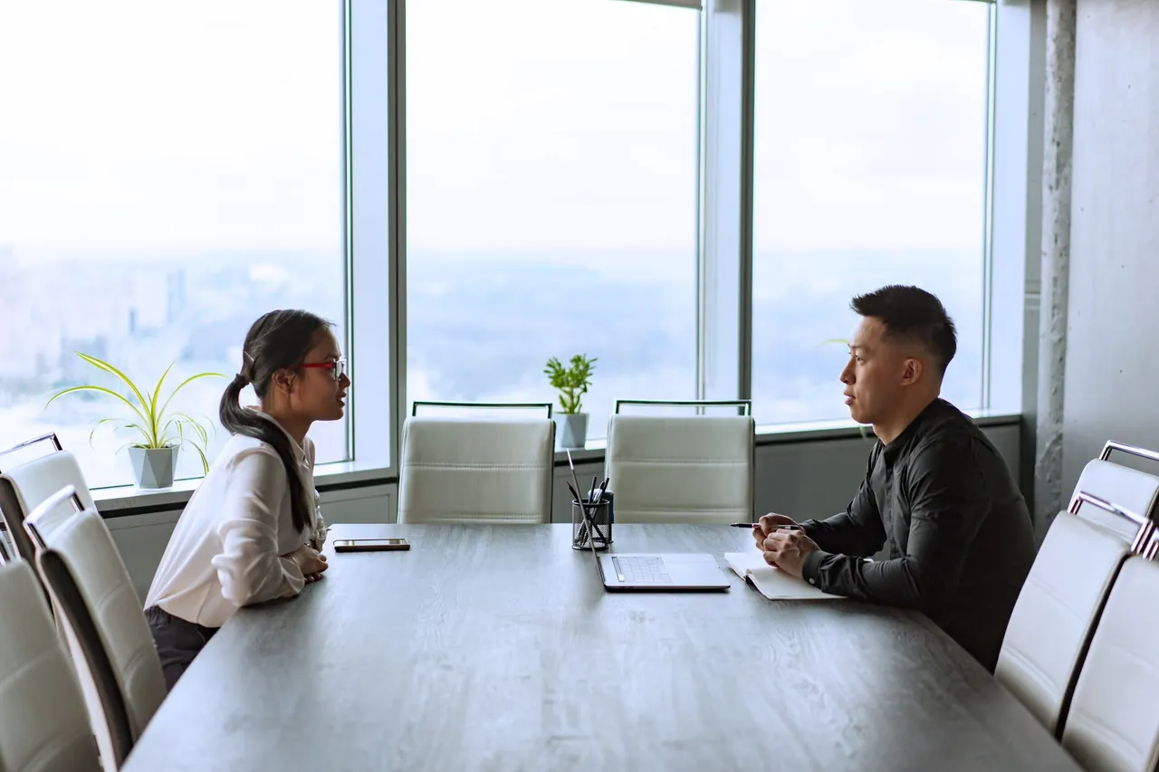 Two professionals talking across a table in a bright office.